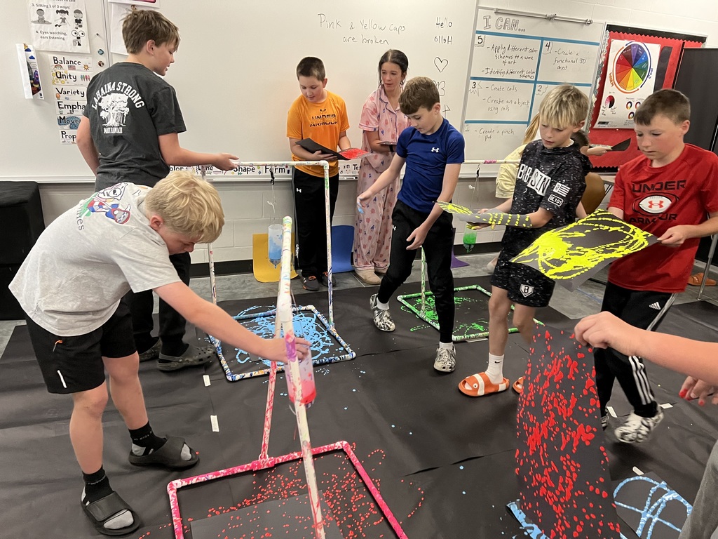 5 boys and 1 girl are standing on black paper while two kids swing paint bottles from a white stand.