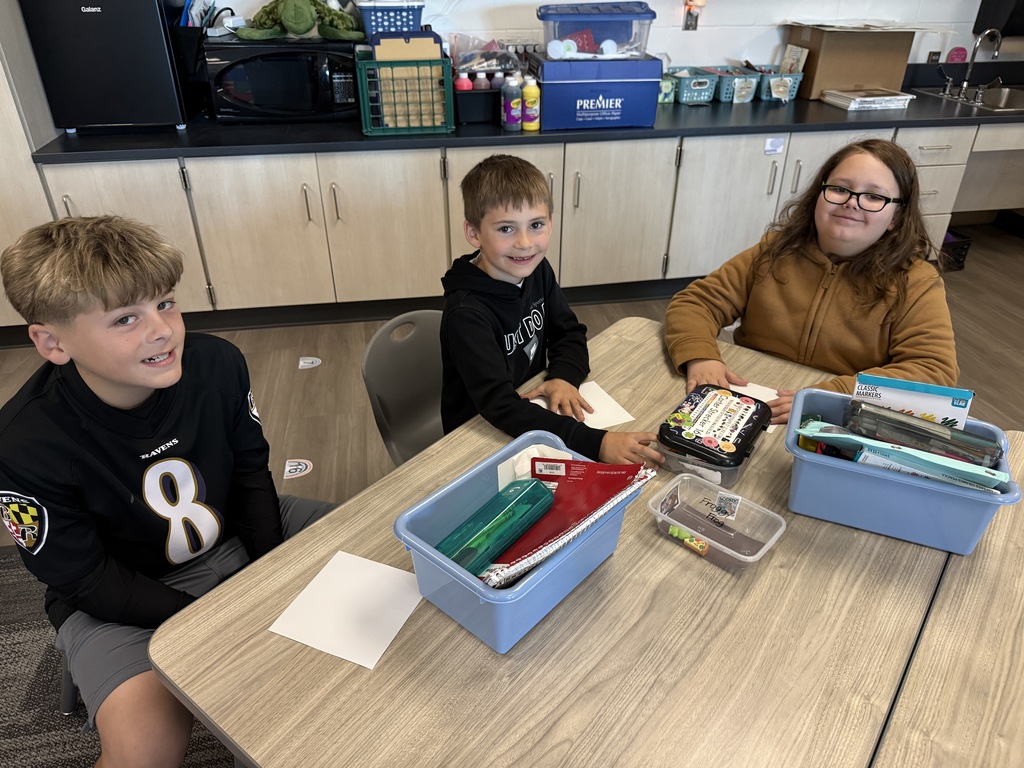 Three boys sit at a table with art supplies and squares to create a kindness picture.
