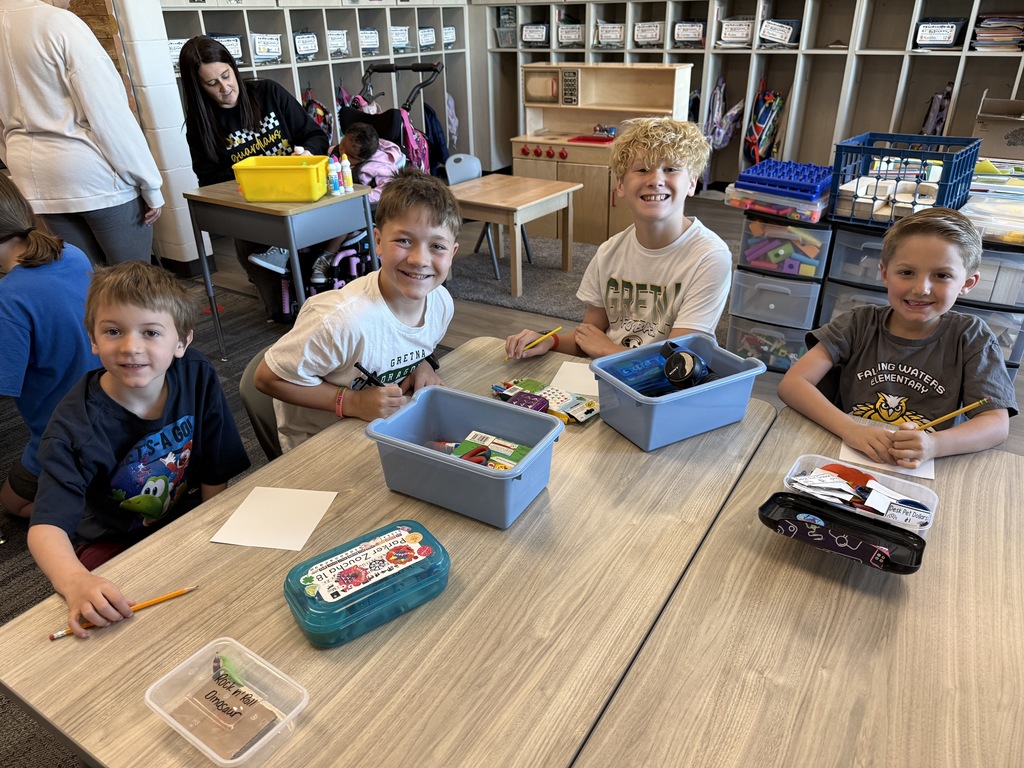 Four boys sit at a table with art supplies and squares to create a kindness picture.