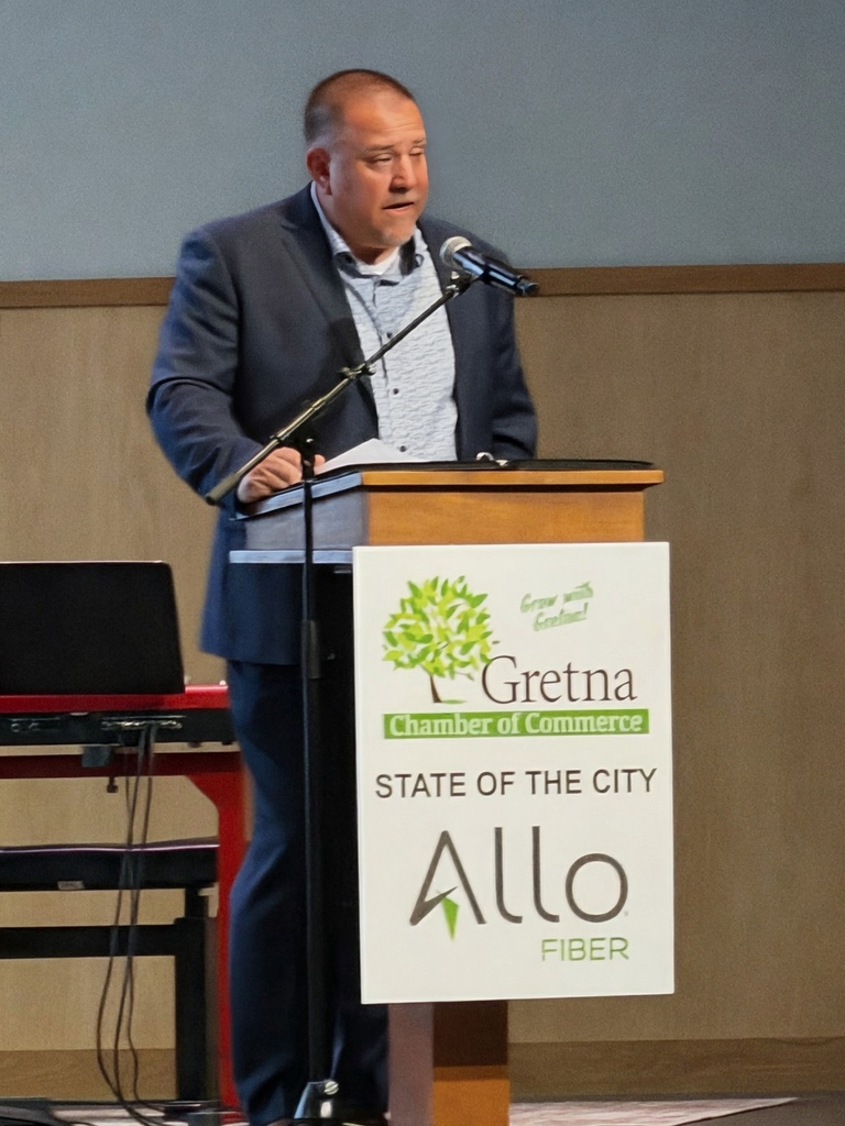 Superintendent Travis Lightle behind a podium speaking at the State of the City hosted by Gretna Chamber of Commerce and ALlo Fiber