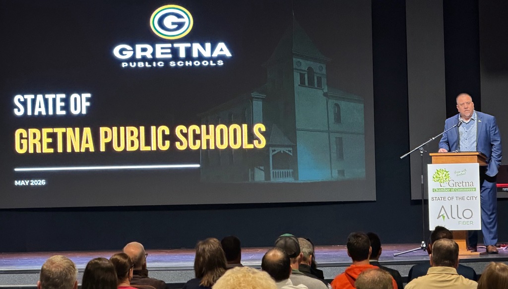 Superintendent Travis Lightle standing behind a podium speaking to the crowd regarding Gretna Public School District