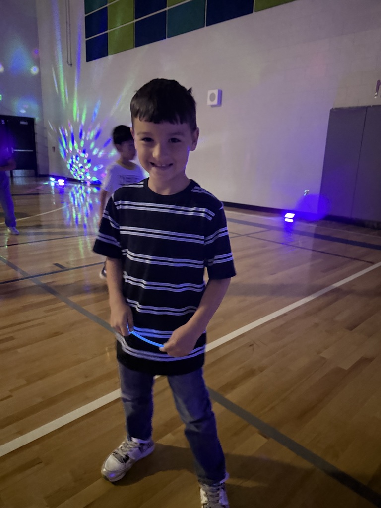 A first grade student smiles for a photo while dancing with his glow stick! 