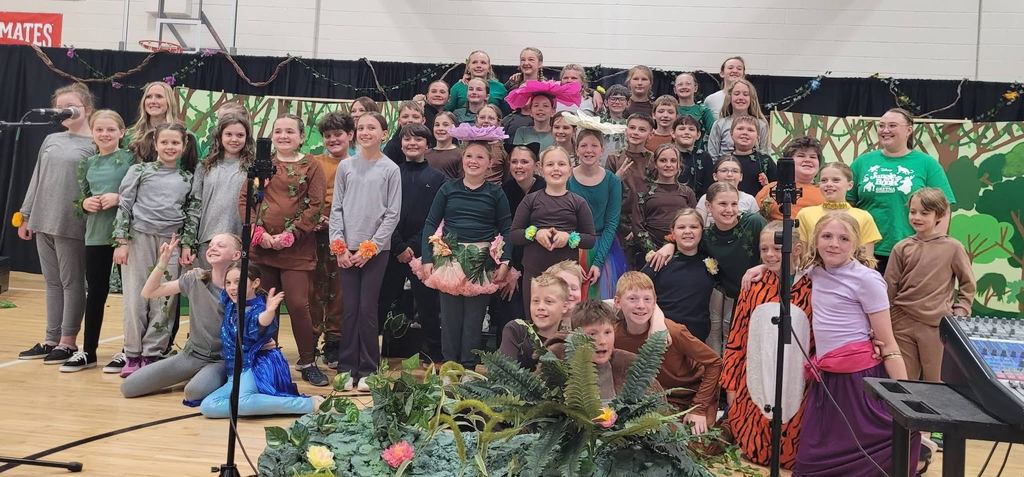A group ensemble photo of the cast in various animal and plant costumes, including tigers, monkeys, and flowers, on the jungle-themed set.