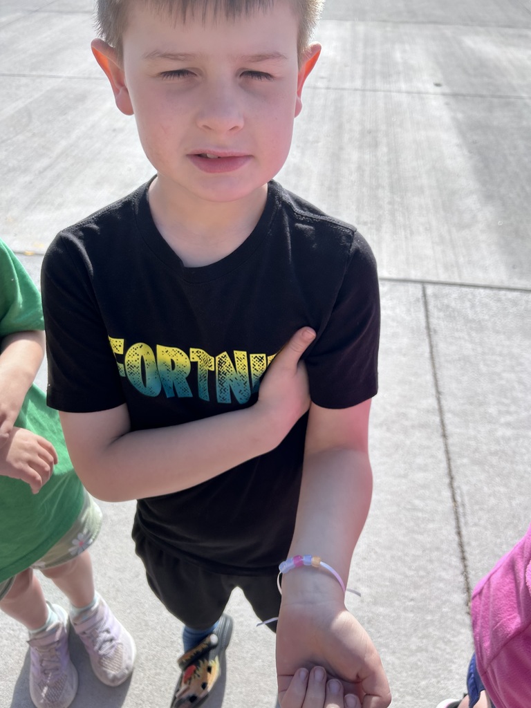 A boy wearing a black "Fortnite" t-shirt holds his arm out to showcase a purple and pink beaded bracelet.
