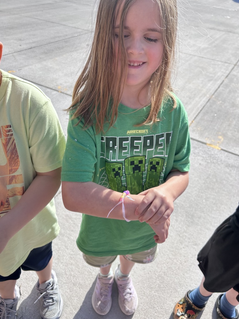 A girl in a green "Creeper" Minecraft t-shirt smiles while looking at a new beaded bracelet on her wrist.