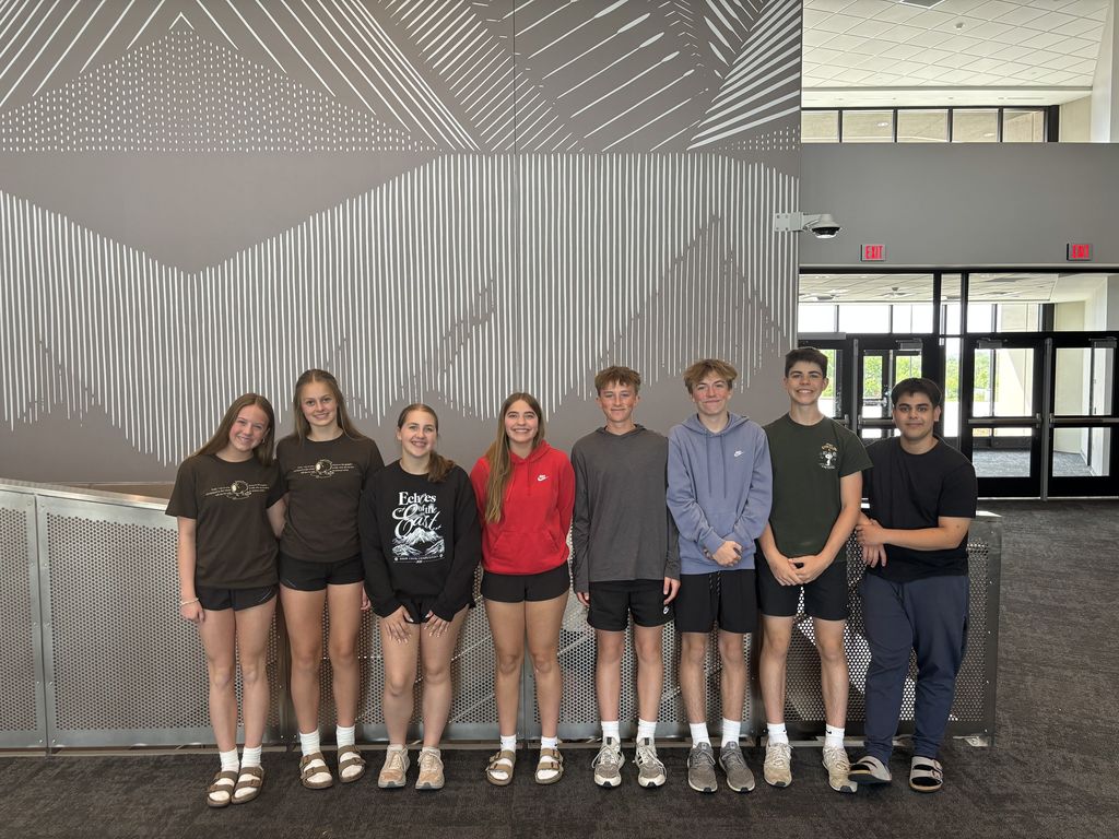 Eight students stand in a hallway and smile at the camera. 