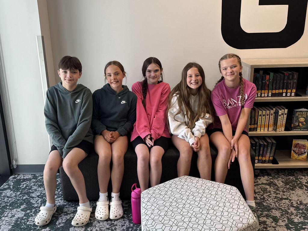 Five students sit on a couch and smile at the camera.