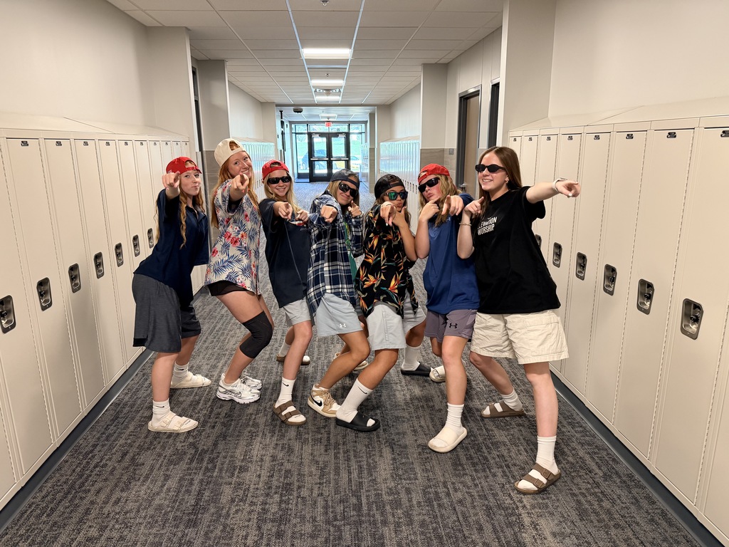 A group of students pose and point at the camera with sunglasses on. 