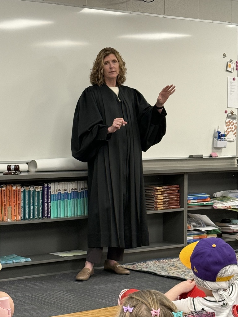 A medium shot of a woman in a black judicial robe gesturing with her hand while speaking in a classroom setting.