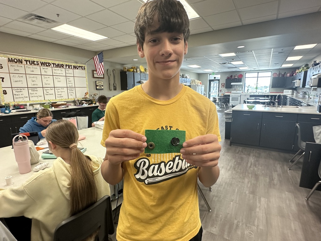 Photo of a male student holding up his scrap of fabric with buttons sewn on.