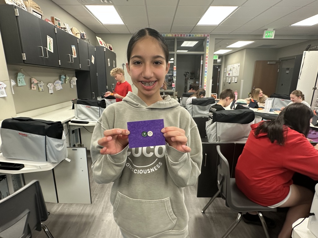 Photo of a female student holding up her scrap of fabric with buttons sewn on.