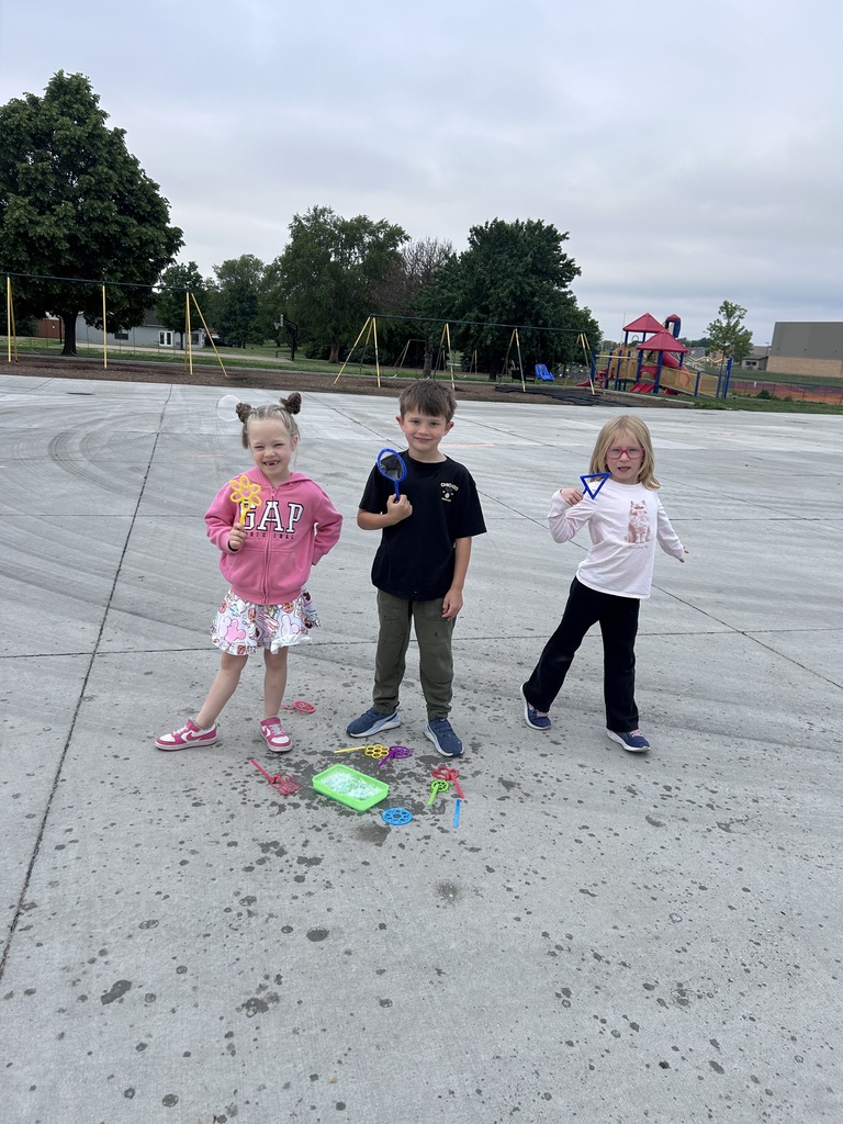 Three children pose for a photo on a spacious concrete playground while holding colorful plastic bubble wands.