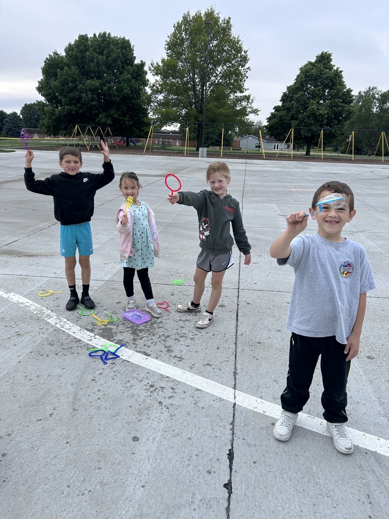 Four children smile and pose on a concrete playground with painted white lines, each holding up a colorful bubble wand.