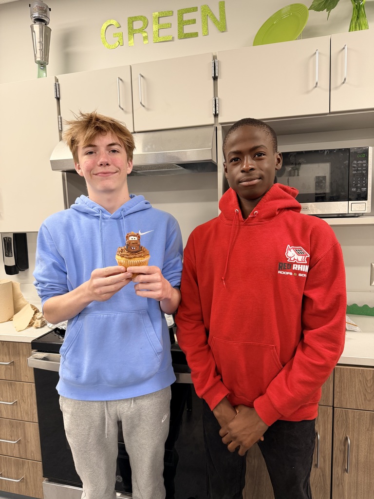 Two boys smile at the camera and hold a cupcake. 