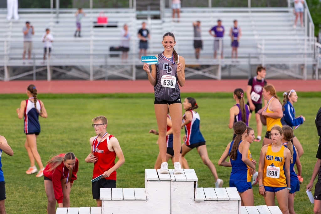 A girl smiles on top of a podium and holds a medal. 