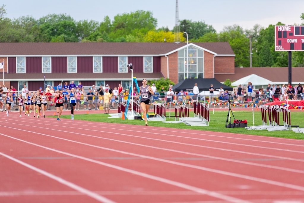 A girl runs on a track and the rest of the group is far behind her. 