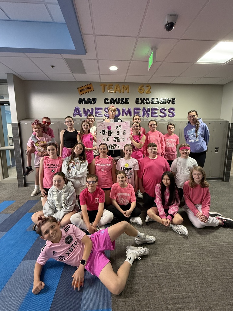 Photo of students and teacher lined up dressed in pink for their kickball game. They are holding a sign that says, "On Tuesdays, we wear pink."