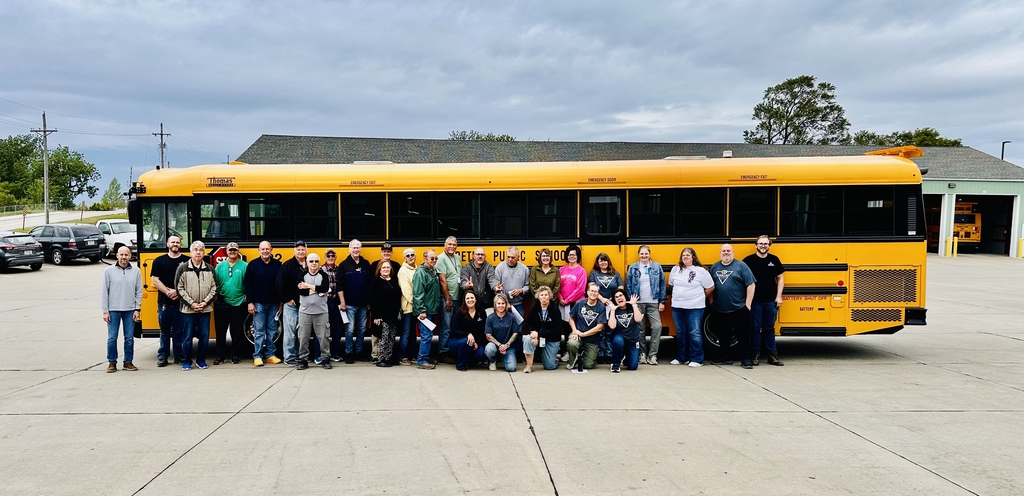 a large group of school bus drivers standing in front of the Gretna Public Schools bus