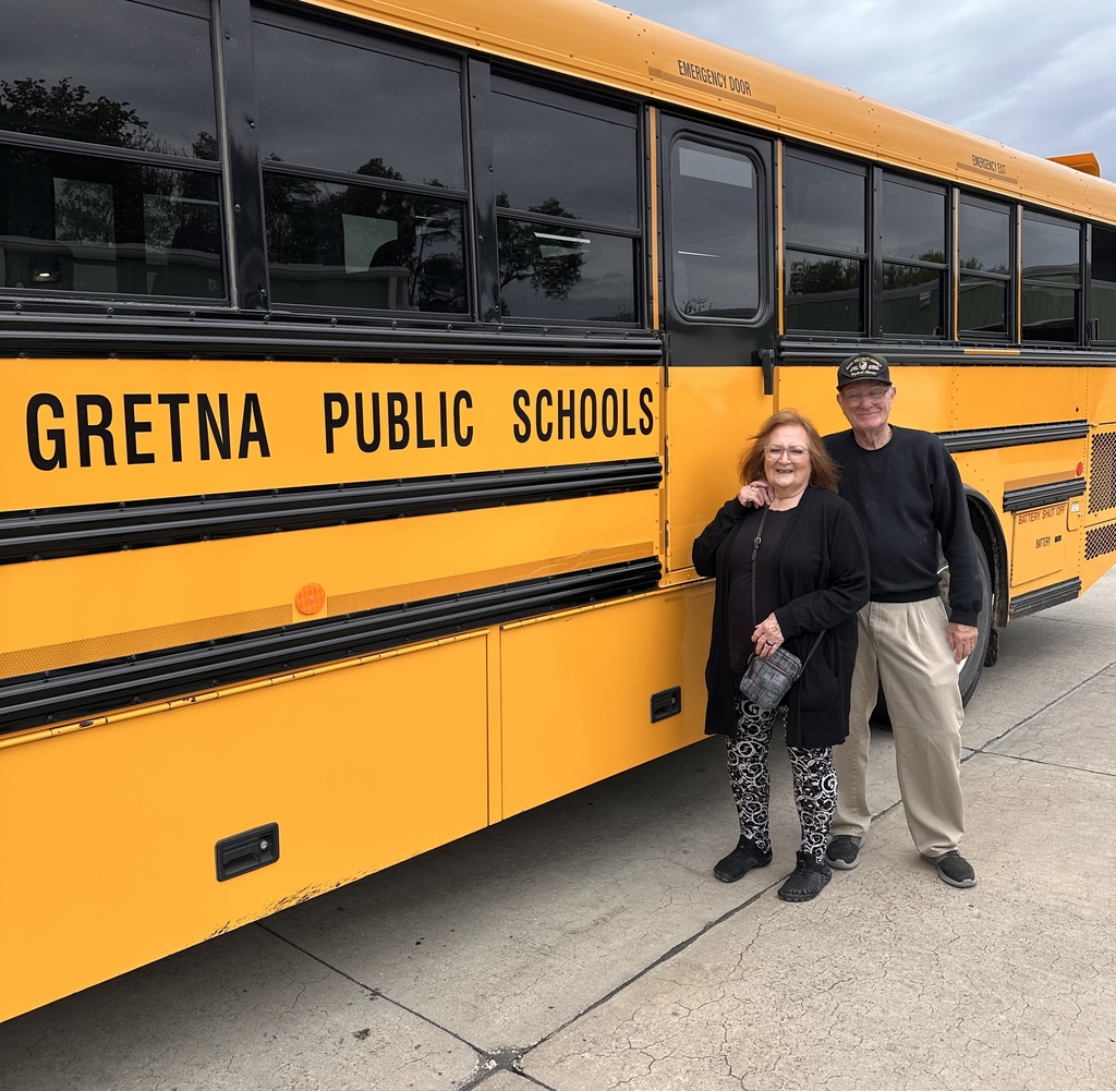 two Gretna Public Schools bus drivers retiring from the transportation department posing in front of the GPS school bus