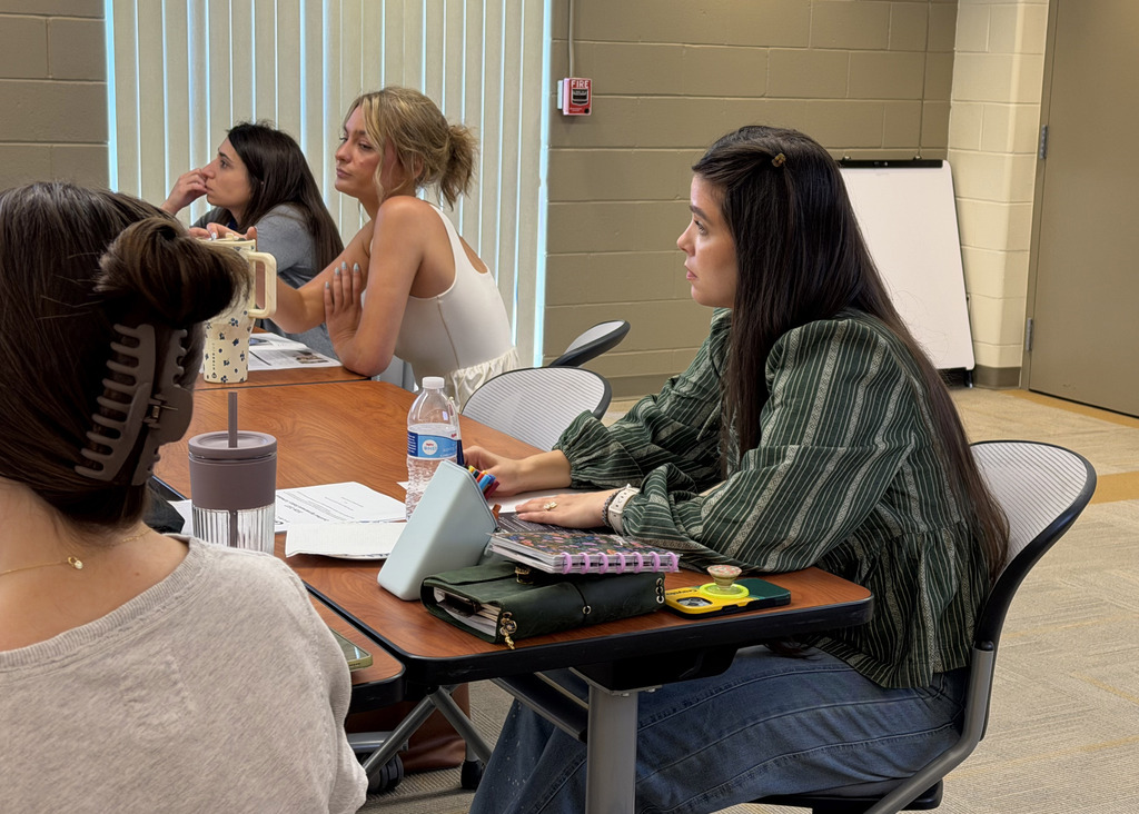 three new hire staff members sitting at a table with their materials on desks in front of them taking notes.