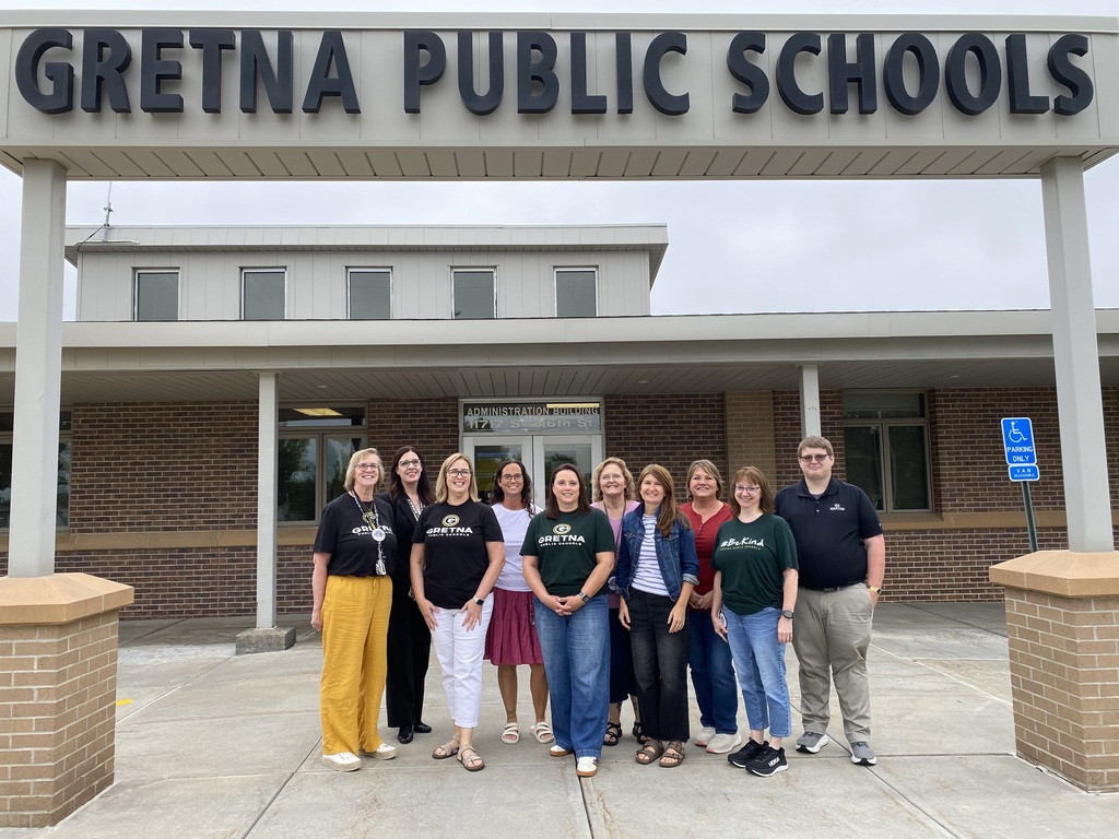 a group of staff members from the district office standing under the "Gretna Public Schools" sign