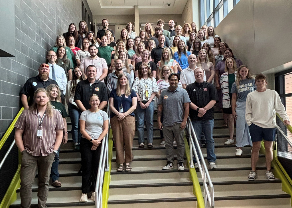 a photo of a large group of new staff members standing on the steps inside of the school