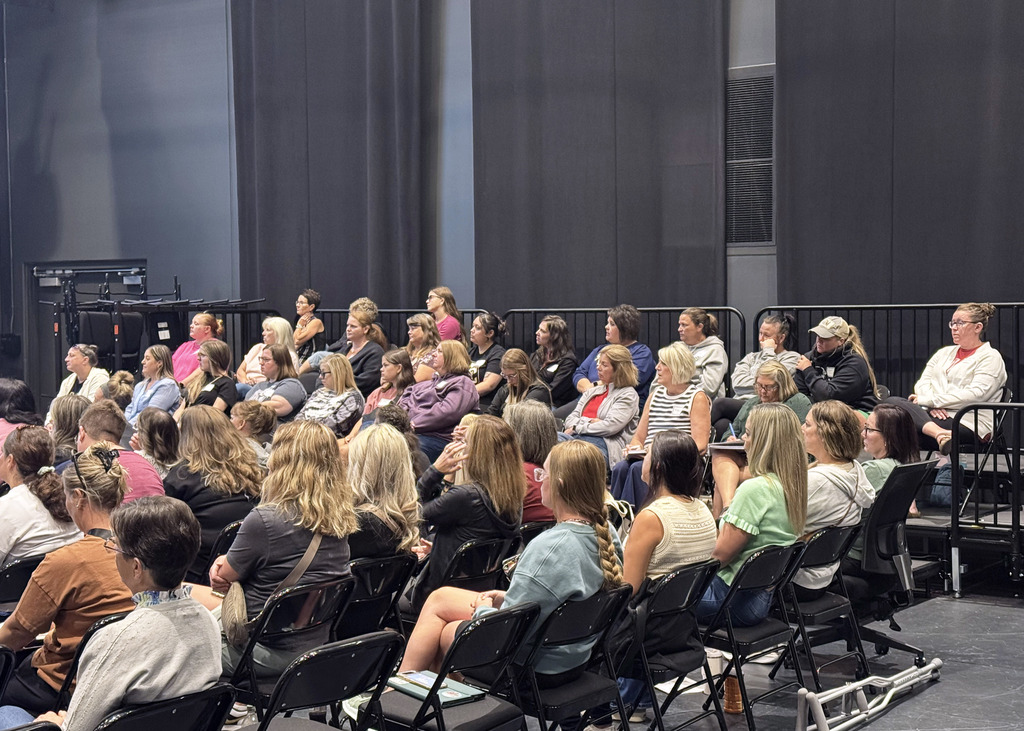 a large group of staff members sitting in chairs engaged in listening and watching presentation.