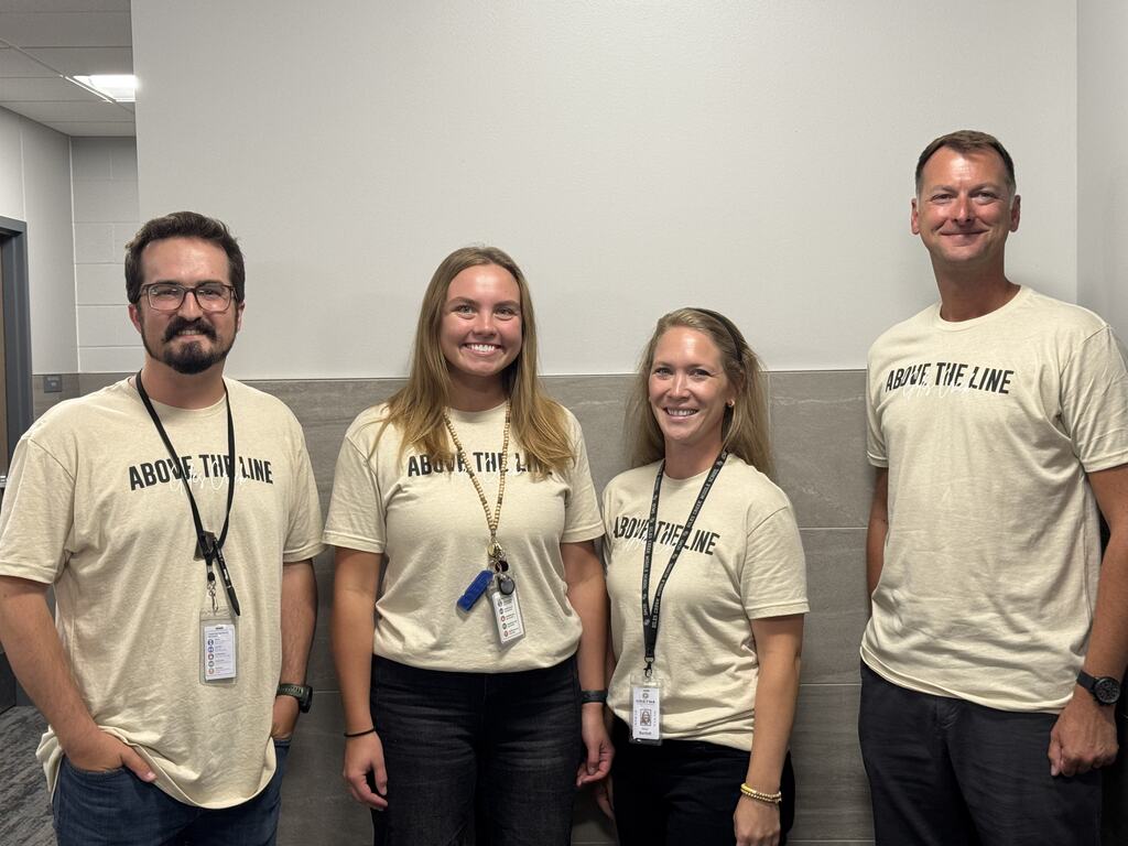 Four adults stand smiling by a wall. 