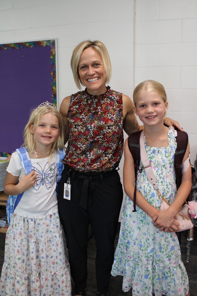 Two sisters stand with Mrs. Conway smiling with their backpacks.