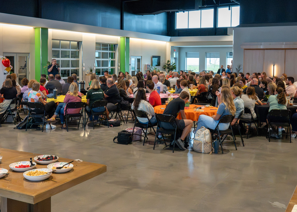 a large room filled with round tables and new staff sitting and enjoying breakfast for Gretna Public Schools