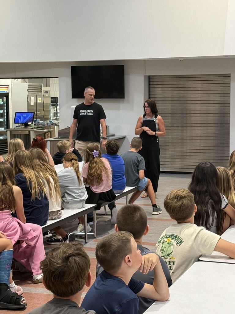 Two adults talking to kids in the lunchroom. 