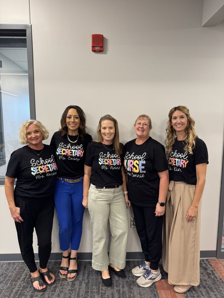 Five women stand against the wall smiling at the camera. 
