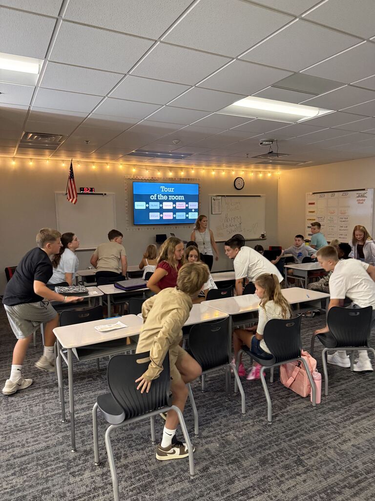 Students sitting at desks in a classroom with a female teacher in front. 