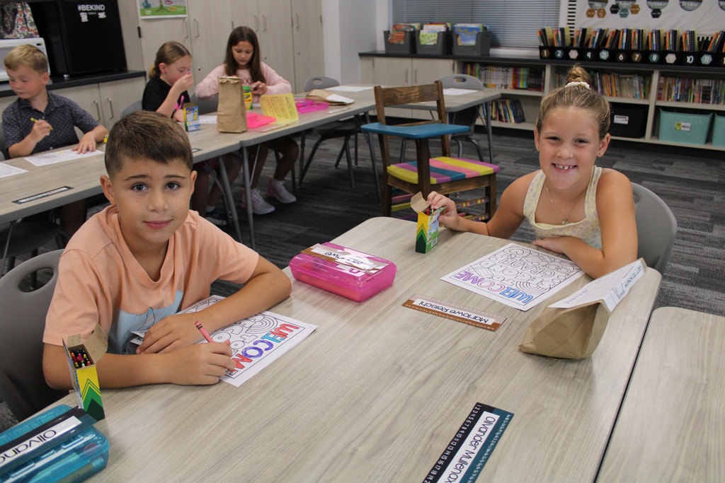 A second grade girl and boy are sitting at a table coloring a worksheet.