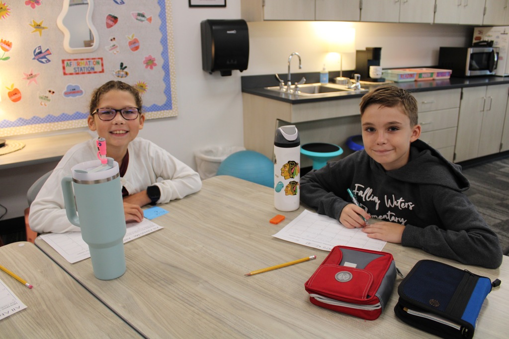 A fifth grade girl and boy are sitting at tables working on a worksheet at the start of the day.