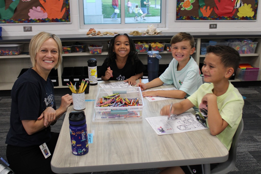 Mrs. Conway sits at a table with three boys who are coloring. Everyone is smiling.