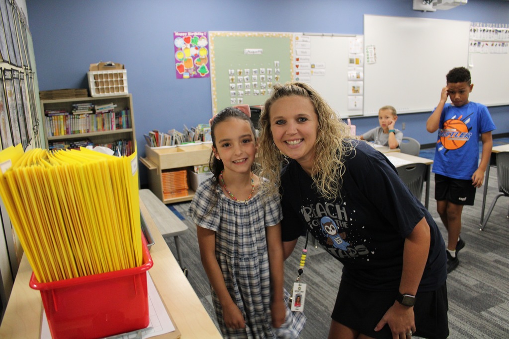 A second grade girl stands with Mrs. Ehlers smiling at the start of the day.