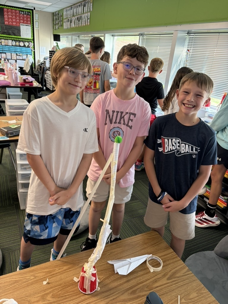 Three boys standing proudly behind a tall paper and red cup tower topped with a green pom-pom.