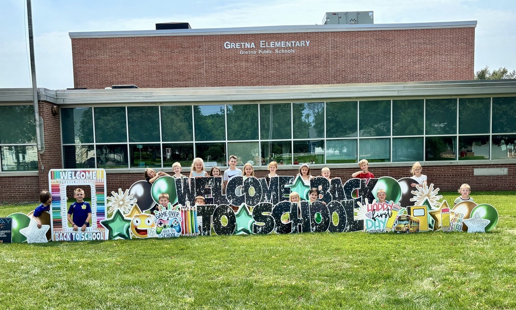 Elementary students gathered behind a colorful "Welcome Back to School" sign on the grass in front of Gretna Elementary.