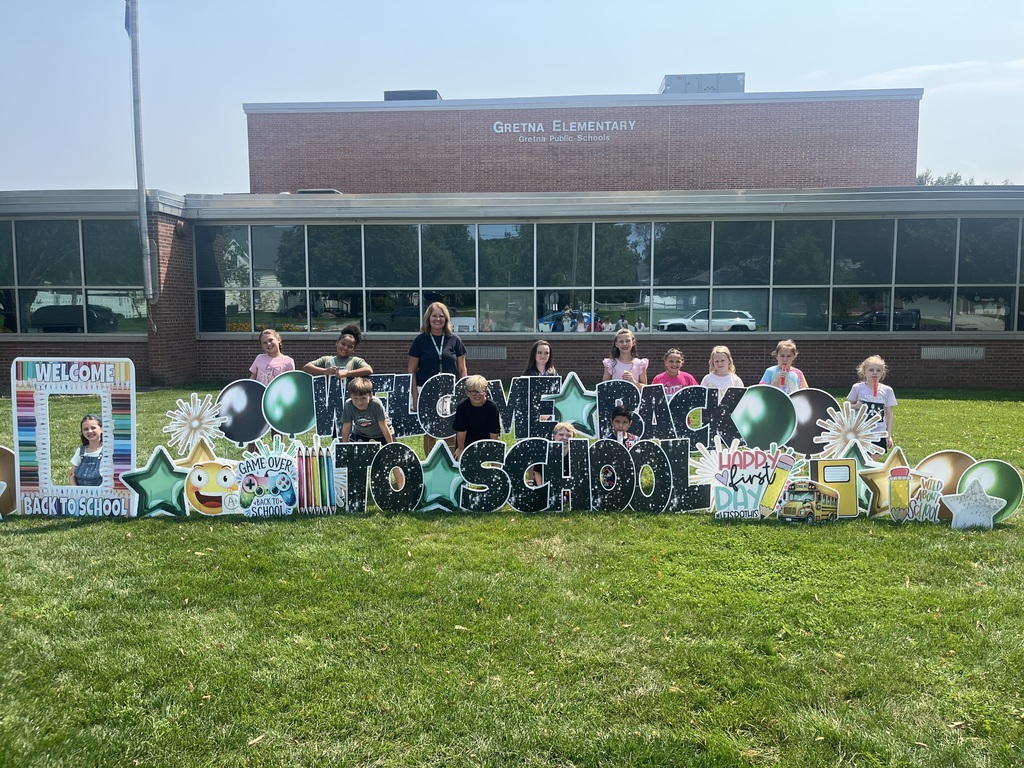A teacher and students posing behind a "Welcome Back to School" lawn sign on the front lawn of Gretna Elementary School.