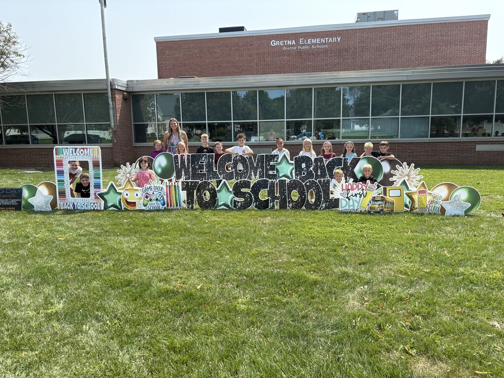 A group of elementary students gathered behind a large "Welcome Back to School" yard sign in front of Gretna Elementary School.