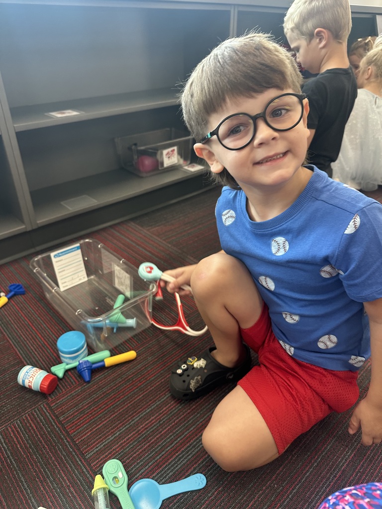 A young boy with glasses kneeling on the classroom floor playing with a plastic doctor kit.