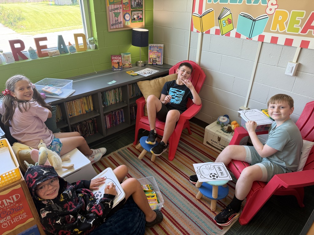 Four students sitting in a cozy classroom reading corner, working on worksheets in colorful lounge chairs and bean bags.