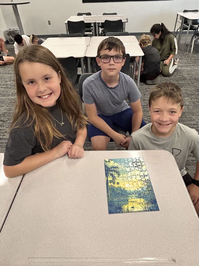 Students smiling at a table with a puzzle. 