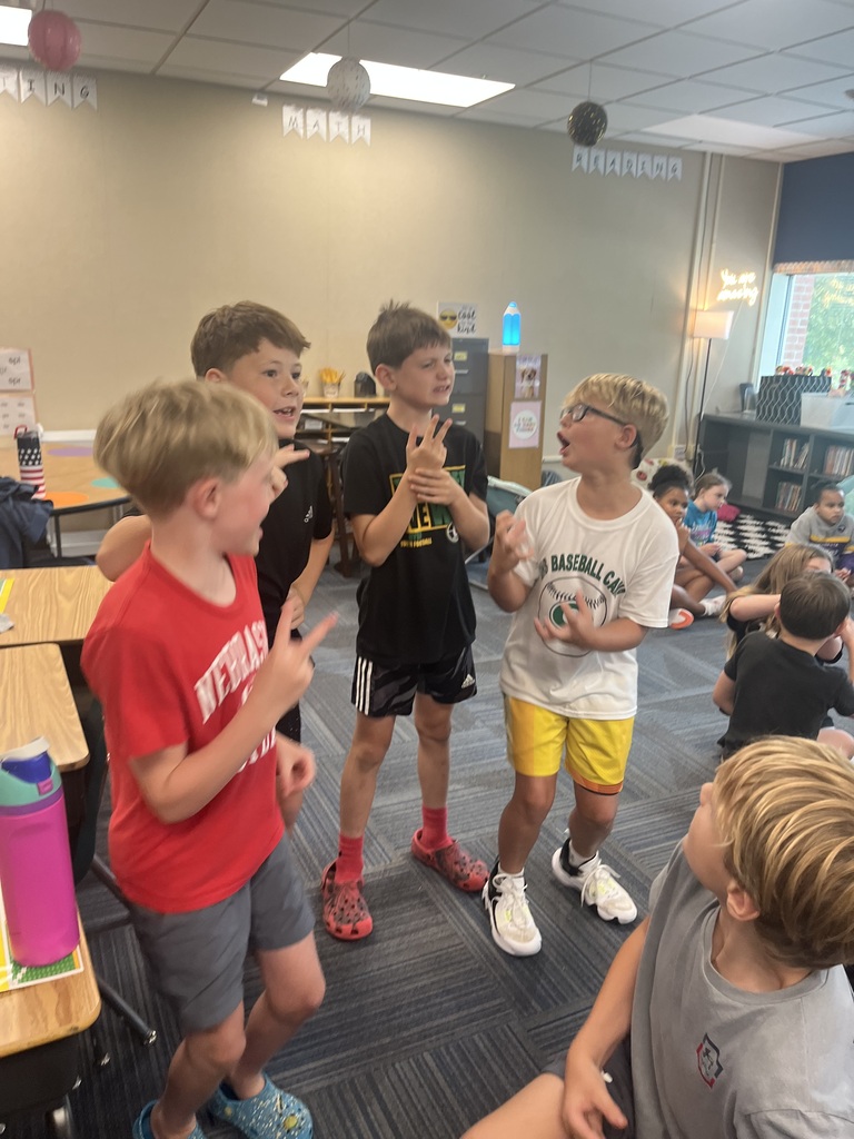 A group of boys stand together in a classroom gesturing and talking animatedly to one another.