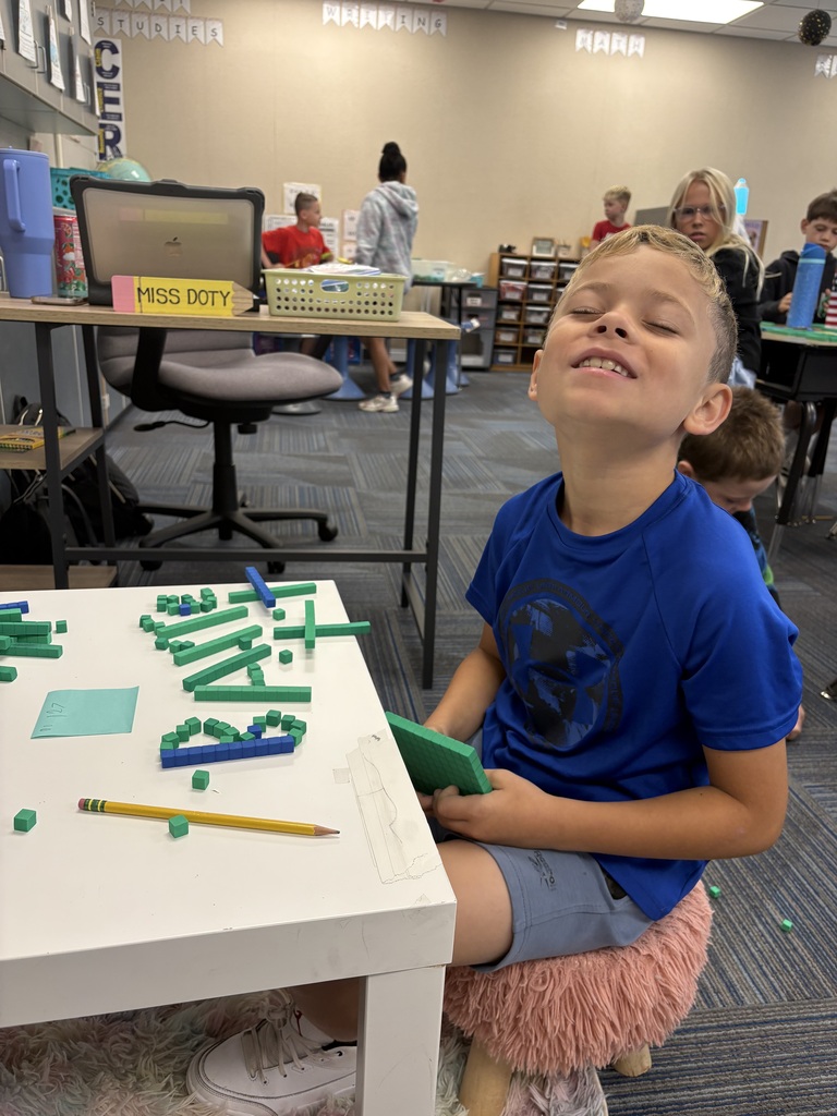 A boy sitting at a low white table with his eyes closed and a big smile, next to base-ten block letters.