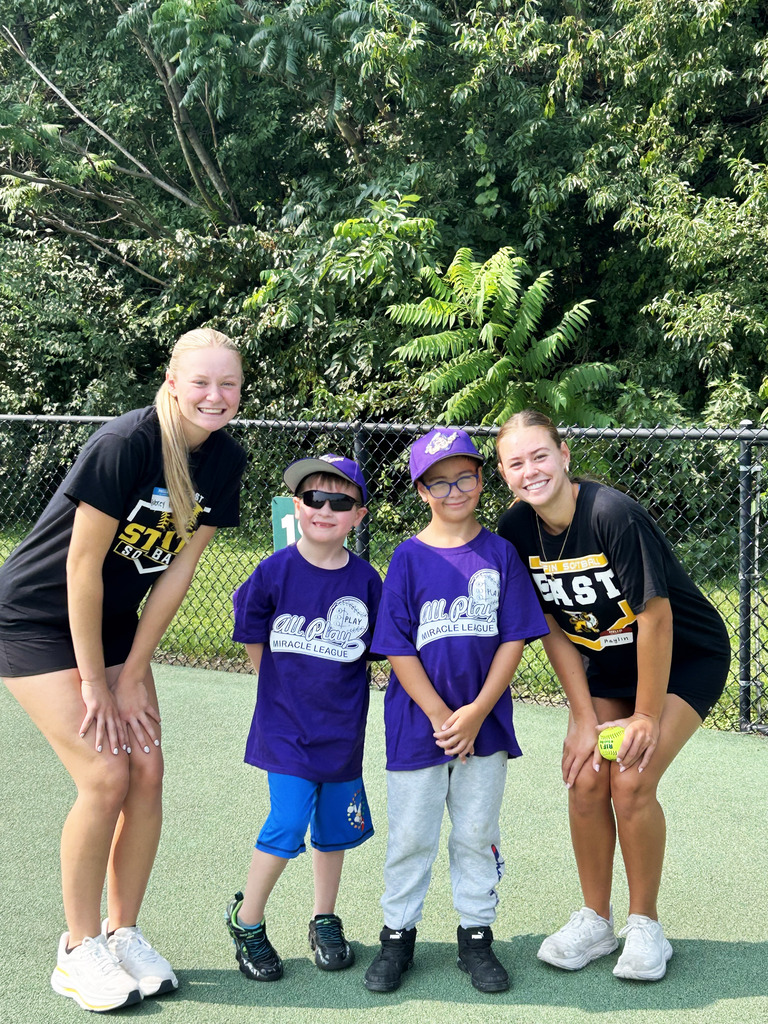 Two Gretna East High School softball players standing with two children outside smiling for the camera