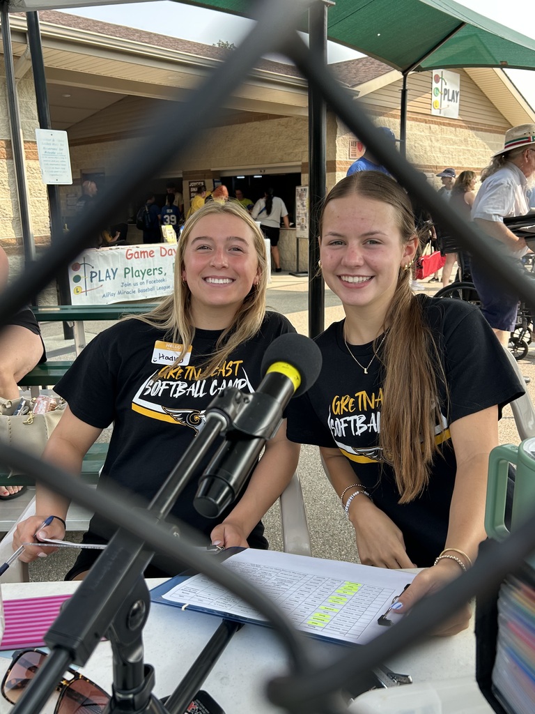two Gretna East High School softball players sitting behind microphones with clipboards on laps
