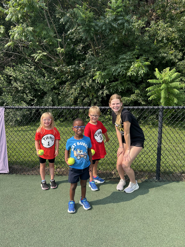 A Gretna East High School student standing with three children outside on the field holding softballs