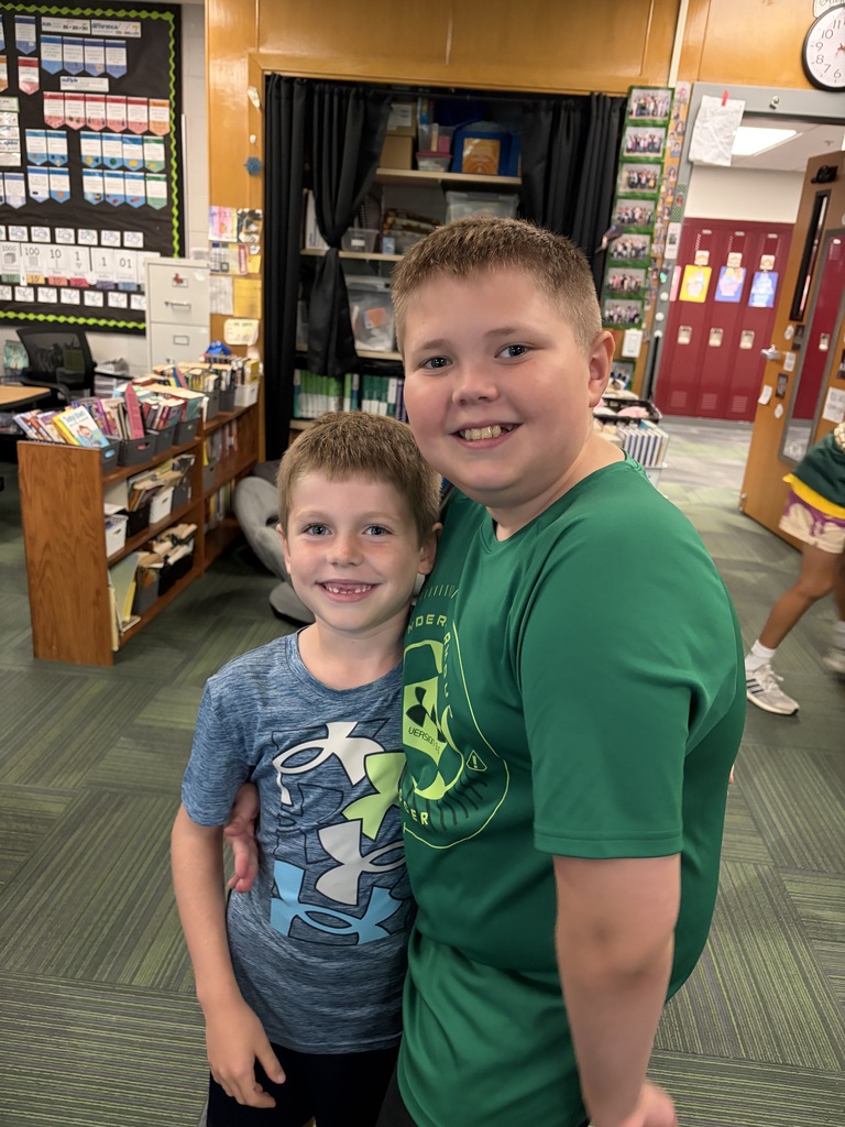 Two young boys smiling, one in a green shirt with his arm around the smaller boy in a blue patterned shirt.